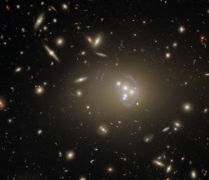 A black background dotted with galaxies. Image center holds a trio of galaxies forming a triangle, with a fourth to the left, and a distinct arc nearly surrounding it.